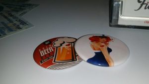 Un pins avec un chope de bière avec un coeur aux couleur rouge, noir et blanc ainsi qu'un pins blanc avec une femme au cheveux orange, une robe bleu et blanche avec une casquette martime et un coeur rouge sur le bras